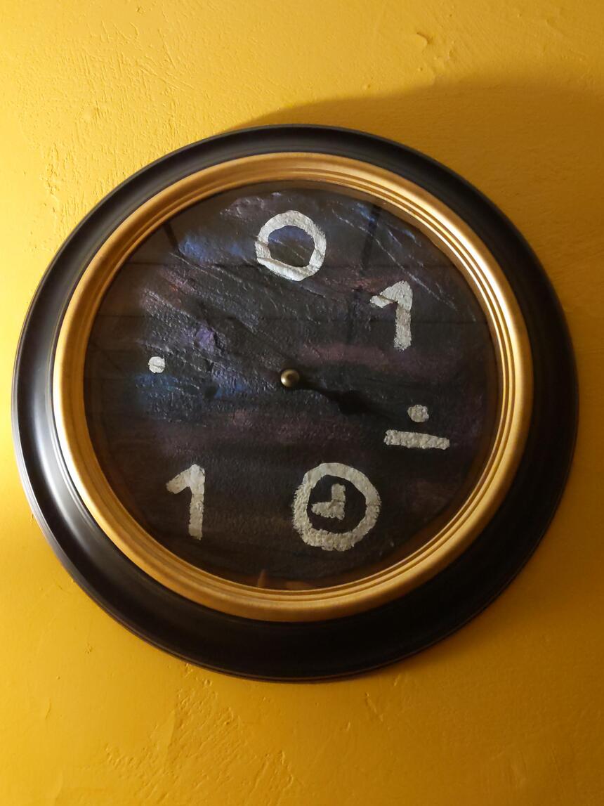 A gold and black framed object with crudely drawn glyphs in white paint.