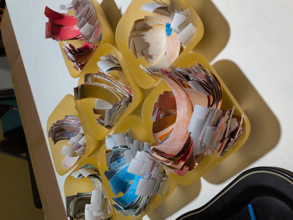 A series of bowls containing torn strips of painted paper.
